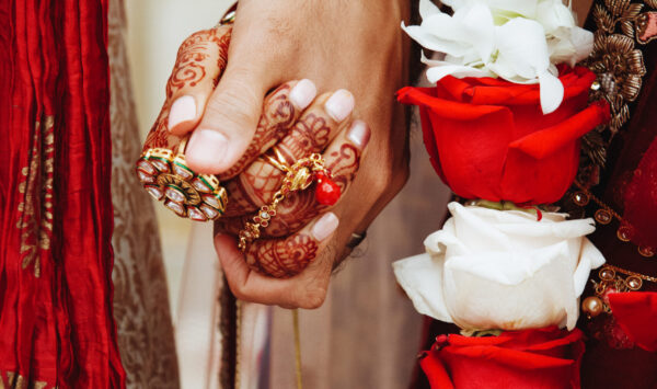 Authentic indian bride and groom's hands holding together in tra Authentic indian bride and groom's hands holding together in traditional wedding attire and red and white roses
